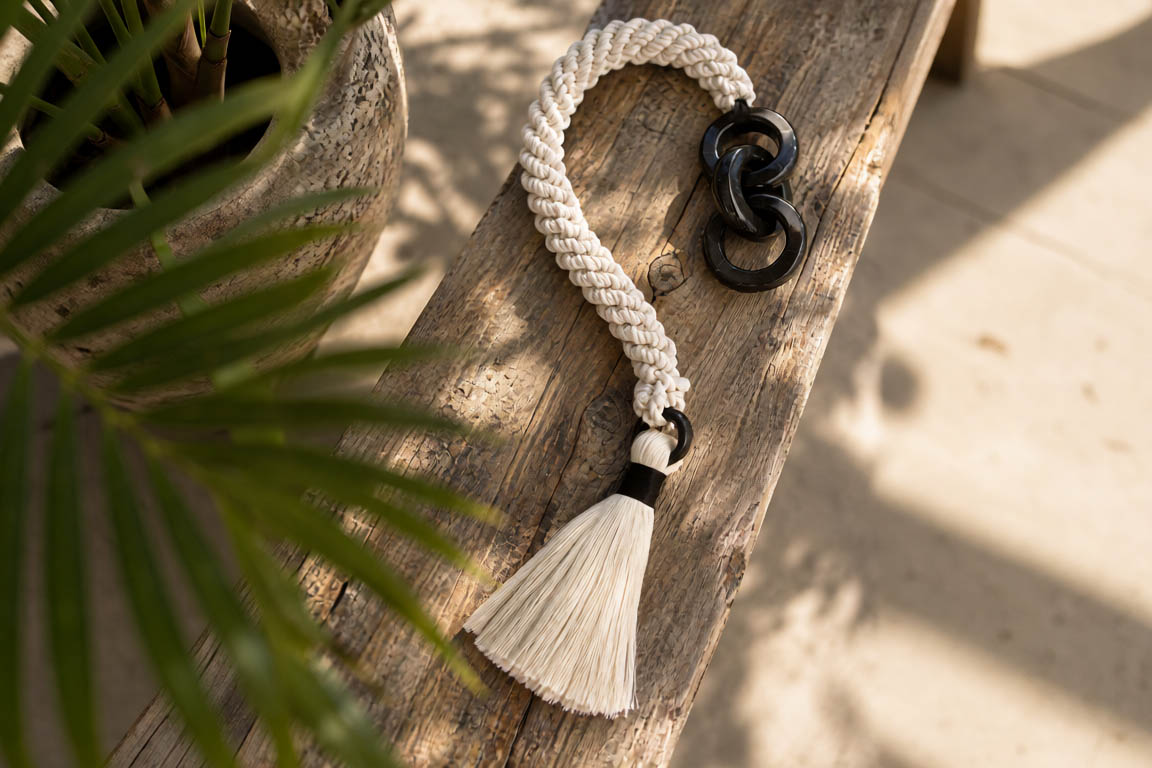 Jengibre Corta Negra, pieza textil artesanal de cordón trenzado color natural con aros negros de mármol, sobre madera.